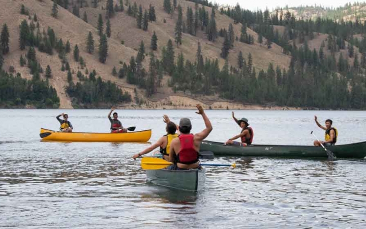 a group of boys in canoes wave at the camera on an outward bound trip